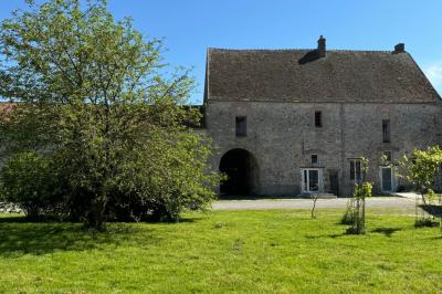 Salle de réception lumineuse avec tables en U décorées de nappes blanches, fleurs et bougies, murs en pierre apparente.