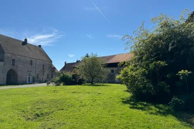 Salle de réception lumineuse avec tables en U décorées de nappes blanches, fleurs et bougies, murs en pierre apparente.