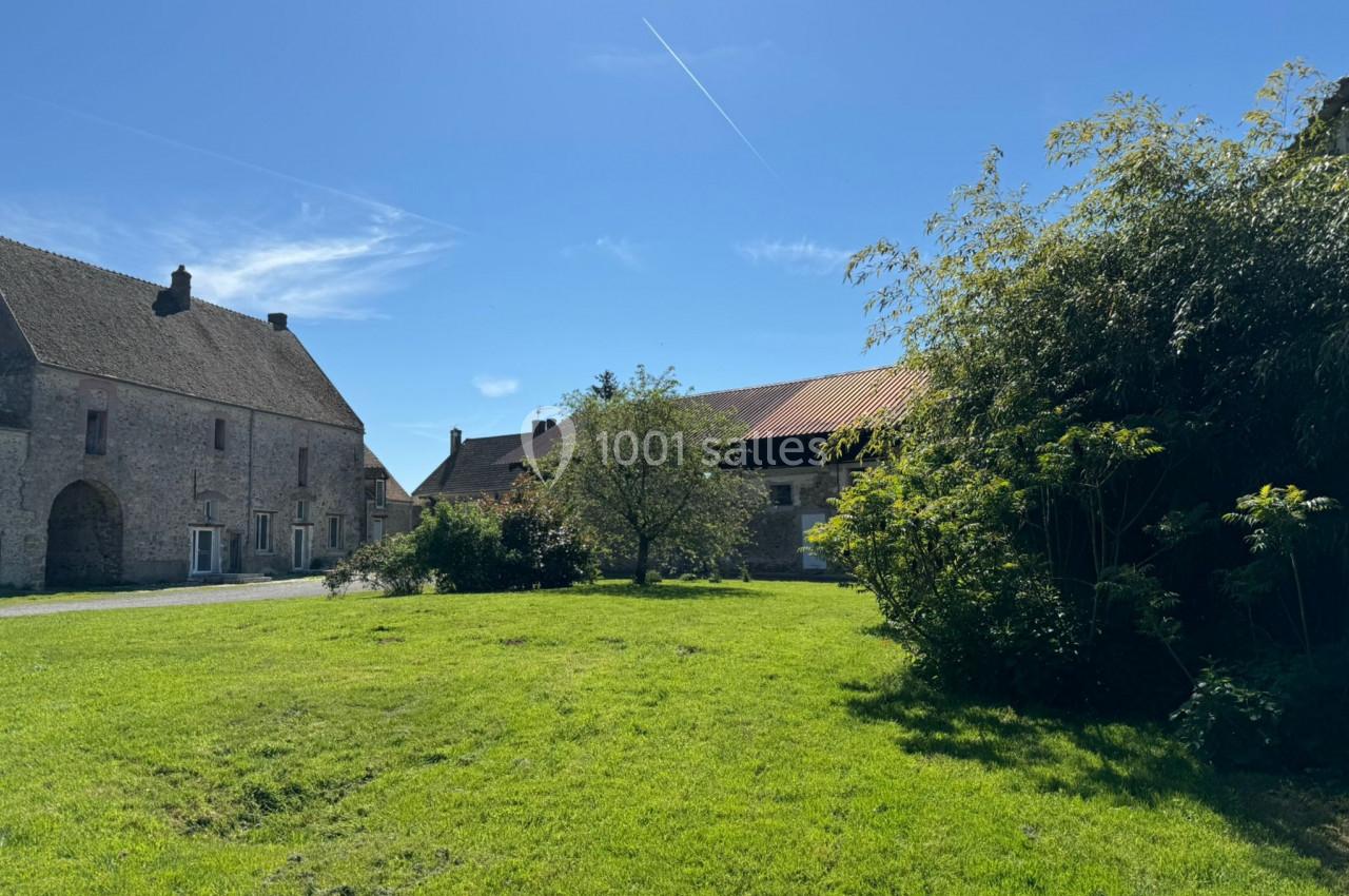 Cour verdoyante entourée de bâtiments en pierre et en bois sous un ciel bleu dégagé.