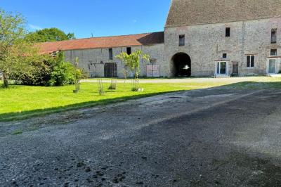 Salle de réception lumineuse avec tables en U décorées de nappes blanches, fleurs et bougies, murs en pierre apparente.