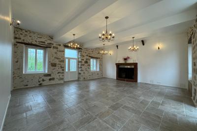 Salle de réception lumineuse avec tables en U décorées de nappes blanches, fleurs et bougies, murs en pierre apparente.
