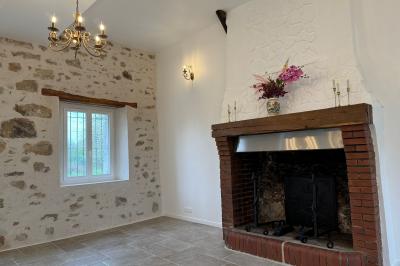 Salle de réception lumineuse avec tables en U décorées de nappes blanches, fleurs et bougies, murs en pierre apparente.