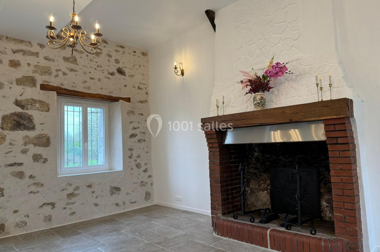 Cheminée en briques avec insert, mur en pierres apparentes, fenêtre à carreaux et lustre dans une pièce lumineuse.