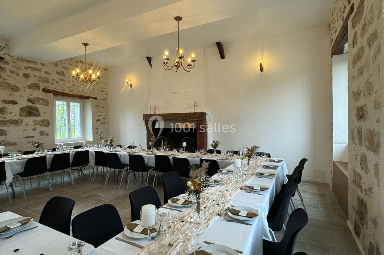 Salle de réception décorée avec des tables longues, nappes claires, vaisselle élégante et chandeliers suspendus.