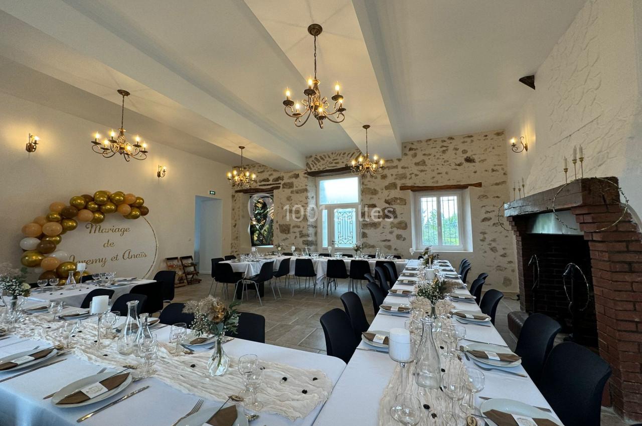 Salle de réception décorée pour un mariage, avec tables dressées, guirlande de ballons et cheminée en pierre.