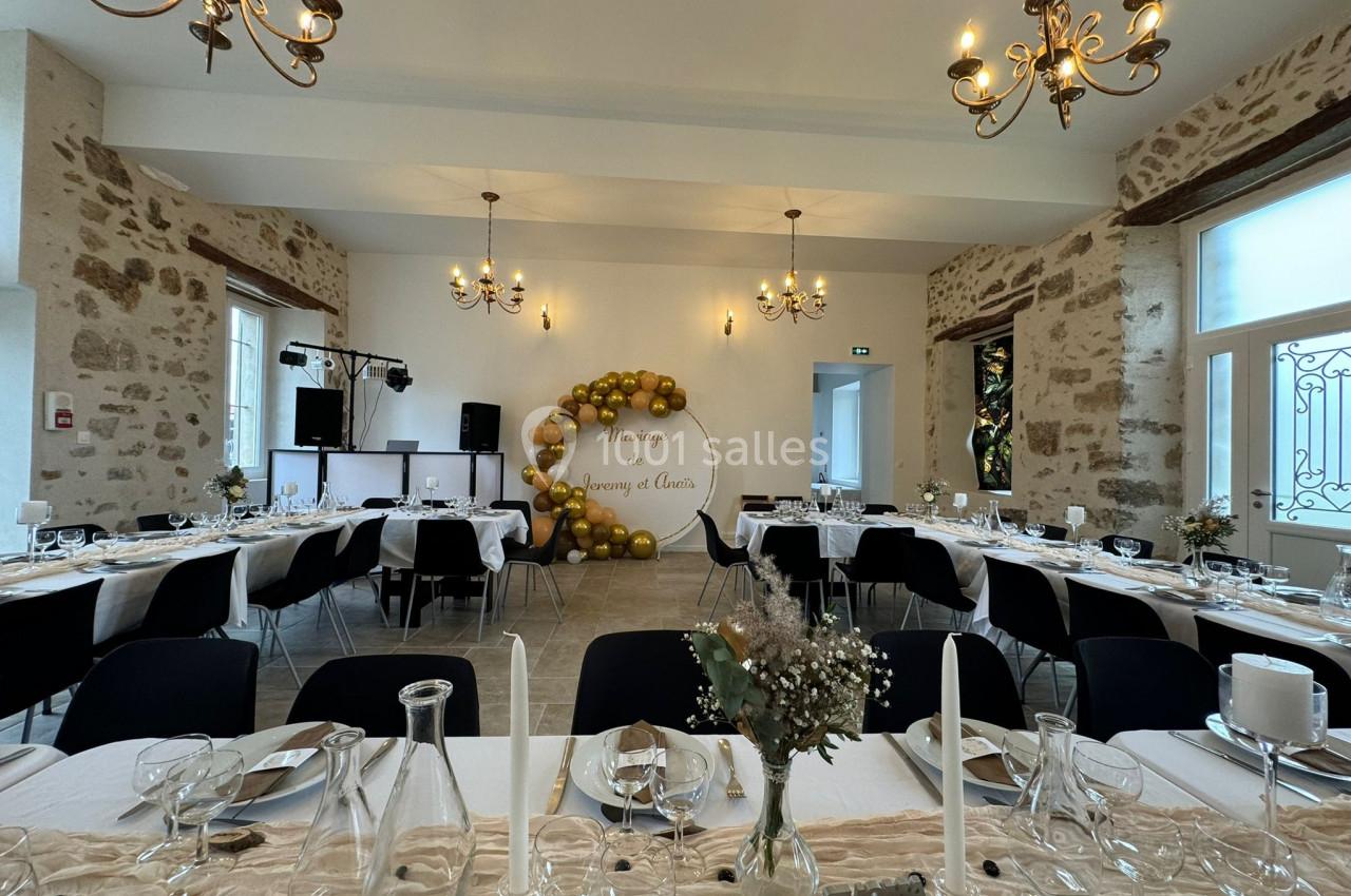 Salle de réception décorée pour un mariage, avec tables dressées, chandeliers au plafond et mur orné de ballons dorés.