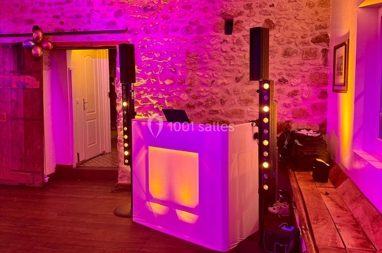 Console de DJ éclairée en blanc et jaune avec enceintes et projecteurs, dans une salle en pierre au décor chaleureux.