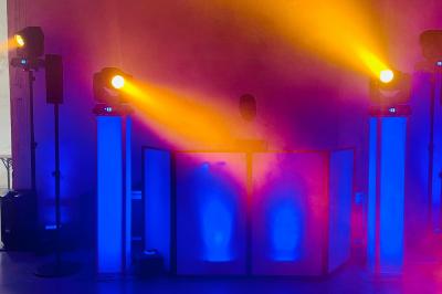 Des invités dansent joyeusement sous des lumières colorées dans une salle décorée pour une fête ou un mariage.