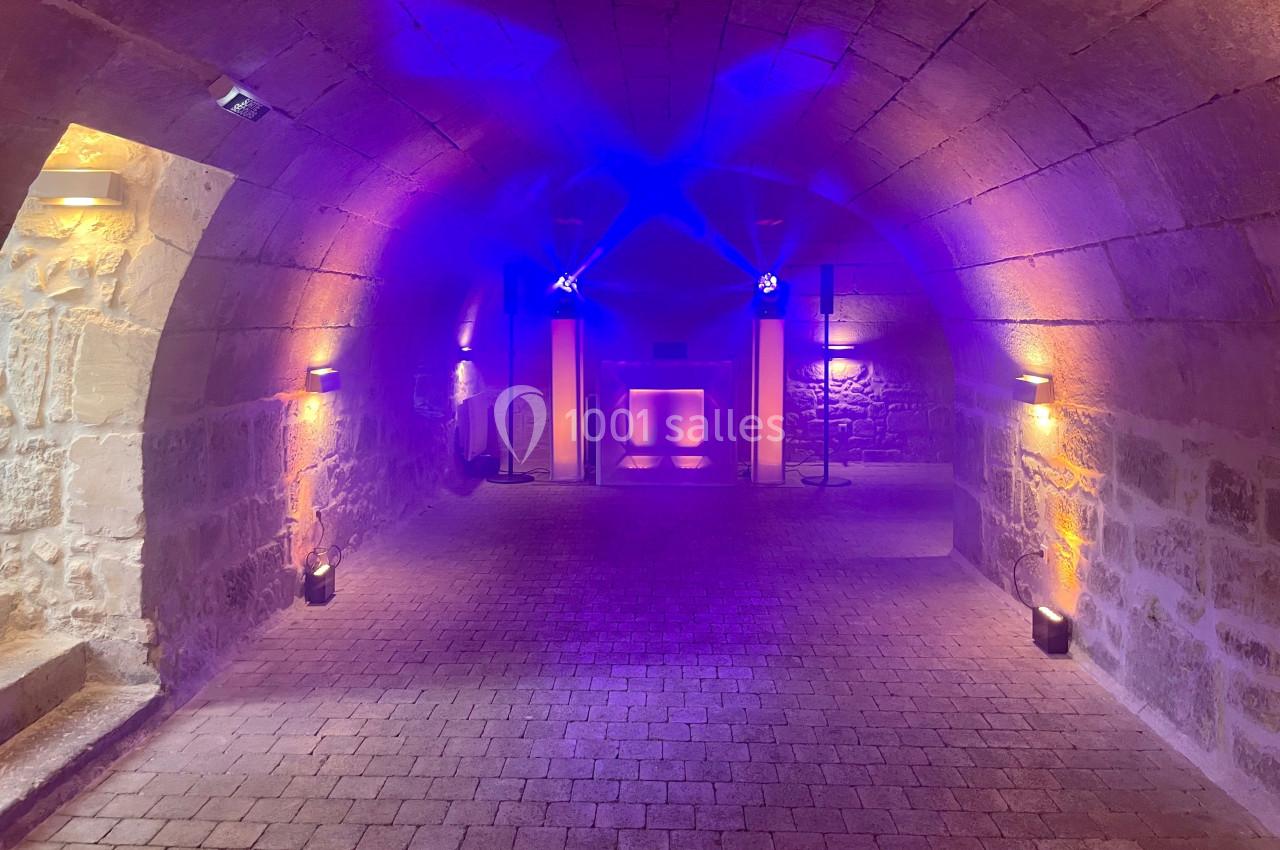 Salle voûtée en pierre éclairée par des lumières colorées, avec une installation lumineuse au fond.
