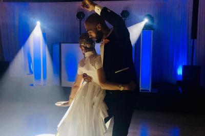 Des invités dansent joyeusement sous des lumières colorées dans une salle décorée pour une fête ou un mariage.