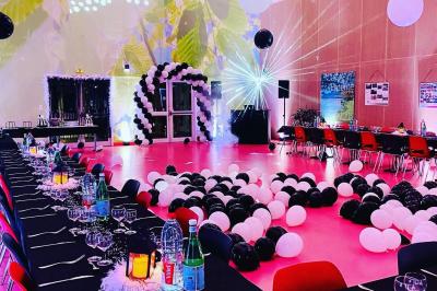 Des invités dansent joyeusement sous des lumières colorées dans une salle décorée pour une fête ou un mariage.