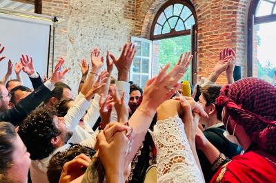 Des invités dansent joyeusement sous des lumières colorées dans une salle décorée pour une fête ou un mariage.