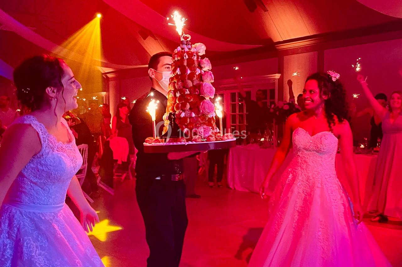 Un serveur apporte une pièce montée décorée de bougies étincelantes lors d'une réception de mariage animée.