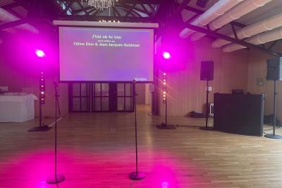 Des invités dansent joyeusement sous des lumières colorées dans une salle décorée pour une fête ou un mariage.