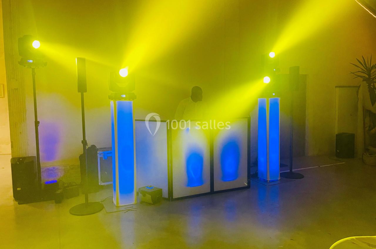 Installation de DJ avec éclairage jaune vif, haut-parleurs et colonnes lumineuses bleues dans une salle.