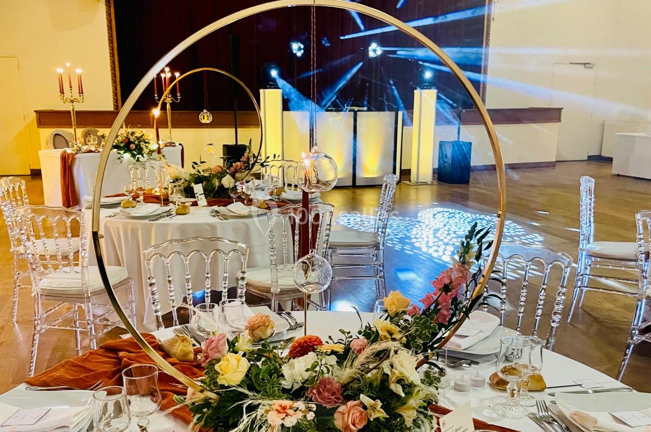 Décoration de table élégante avec fleurs colorées et cercle doré, dans une salle de réception illuminée.