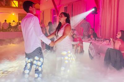 Des invités dansent joyeusement sous des lumières colorées dans une salle décorée pour une fête ou un mariage.