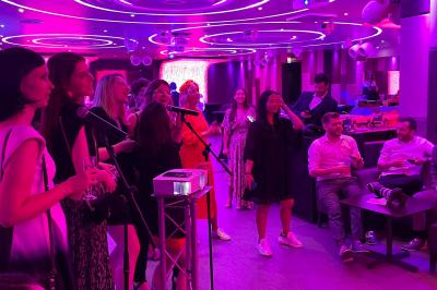 Des invités dansent joyeusement sous des lumières colorées dans une salle décorée pour une fête ou un mariage.