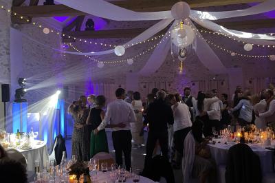 Des invités dansent joyeusement sous des lumières colorées dans une salle décorée pour une fête ou un mariage.