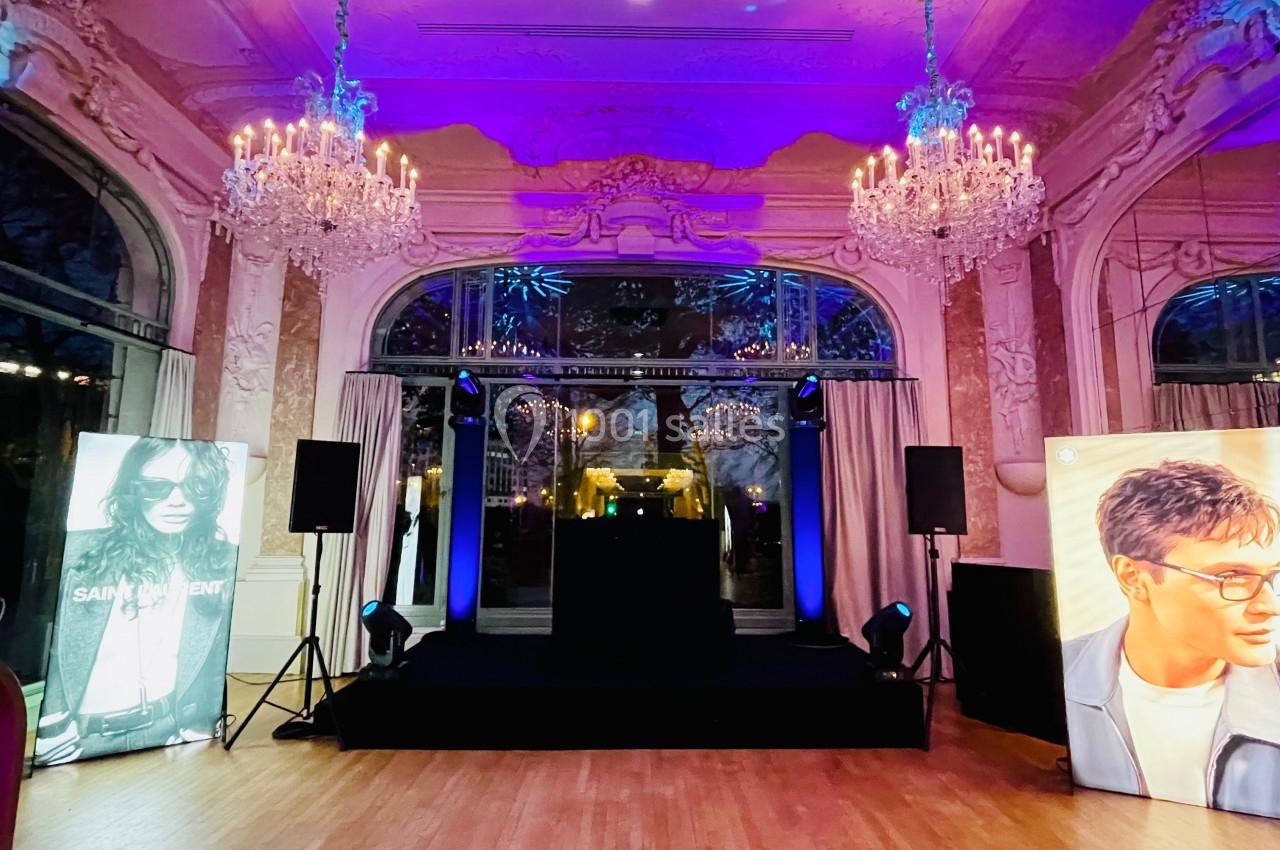 Salle élégante avec lustres, scène centrale éclairée et affiches de mannequins de chaque côté.