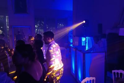Des invités dansent joyeusement sous des lumières colorées dans une salle décorée pour une fête ou un mariage.