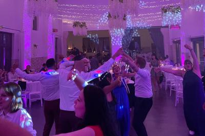 Des invités dansent joyeusement sous des lumières colorées dans une salle décorée pour une fête ou un mariage.