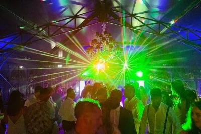 Personnes dansant sous des jeux de lumière colorés dans une salle avec un lustre et une structure métallique visible.