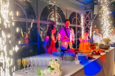 Des convives célèbrent autour d'une table décorée, avec des étincelles et des desserts dans une ambiance festive.