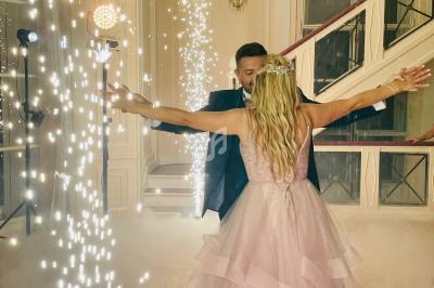 Un couple danse au milieu d'effets lumineux et de fumée dans une salle élégante avec escalier en arrière-plan.