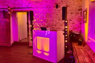 Console de DJ éclairée en blanc entourée de colonnes lumineuses dans une salle en pierre avec éclairage d'ambiance violet.