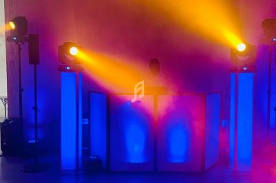 Un DJ mixe derrière une table éclairée en bleu, entourée de projecteurs diffusant des lumières jaunes et rouges.