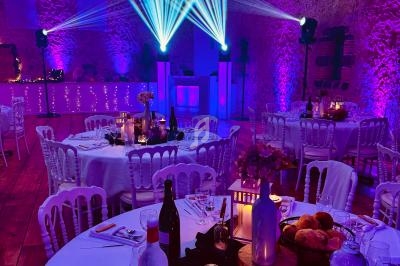 Salle de réception décorée avec des tables rondes, éclairage violet et projecteurs lumineux.