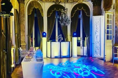 Salle de réception élégante avec parquet, lustre, rideaux dorés et éclairage coloré projeté au sol.