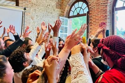 Groupe de personnes levant les bras en l'air dans une ambiance festive, près de fenêtres et d'un mur en briques.