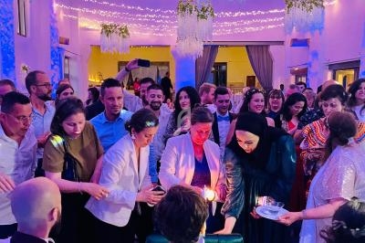 Un groupe de personnes allume des bougies dans une salle décorée avec des guirlandes lumineuses et des plantes suspendues.