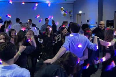 Des personnes dansent et s'amusent sous des lumières colorées dans une salle décorée de ballons.