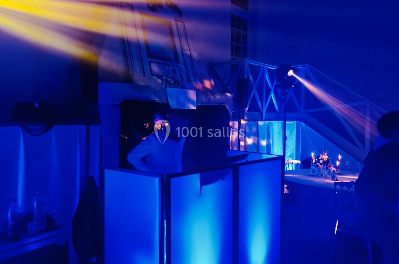 Une personne se tient derrière une console éclairée de lumières bleues dans une ambiance de soirée avec projecteurs colorés.