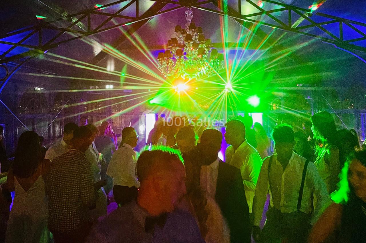 Personnes dansant sous des jeux de lumière colorés dans une salle avec une structure métallique et un lustre central.