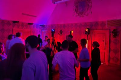 Des invités dansent joyeusement sous des lumières colorées dans une salle décorée pour une fête ou un mariage.