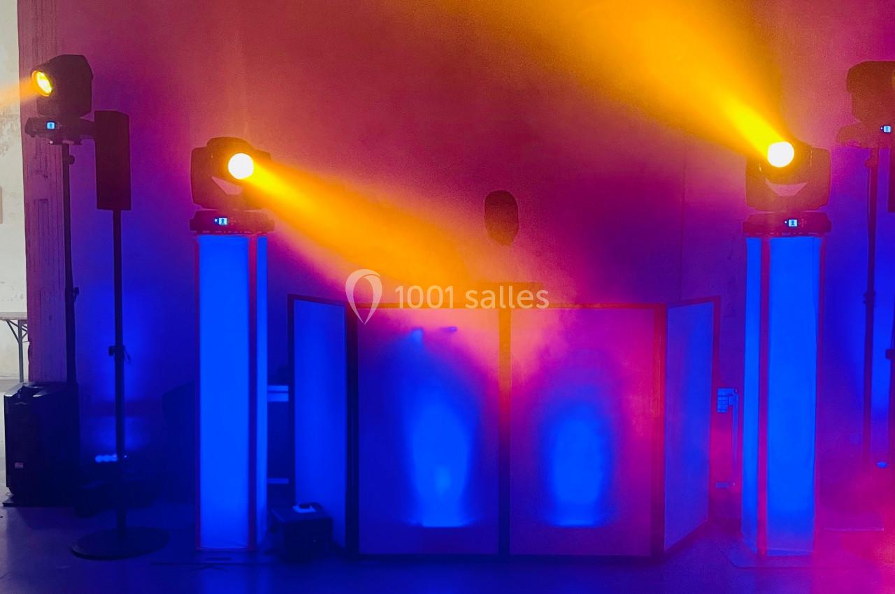 Un DJ mixe derrière une table éclairée de lumières bleues et jaunes dans une ambiance festive.