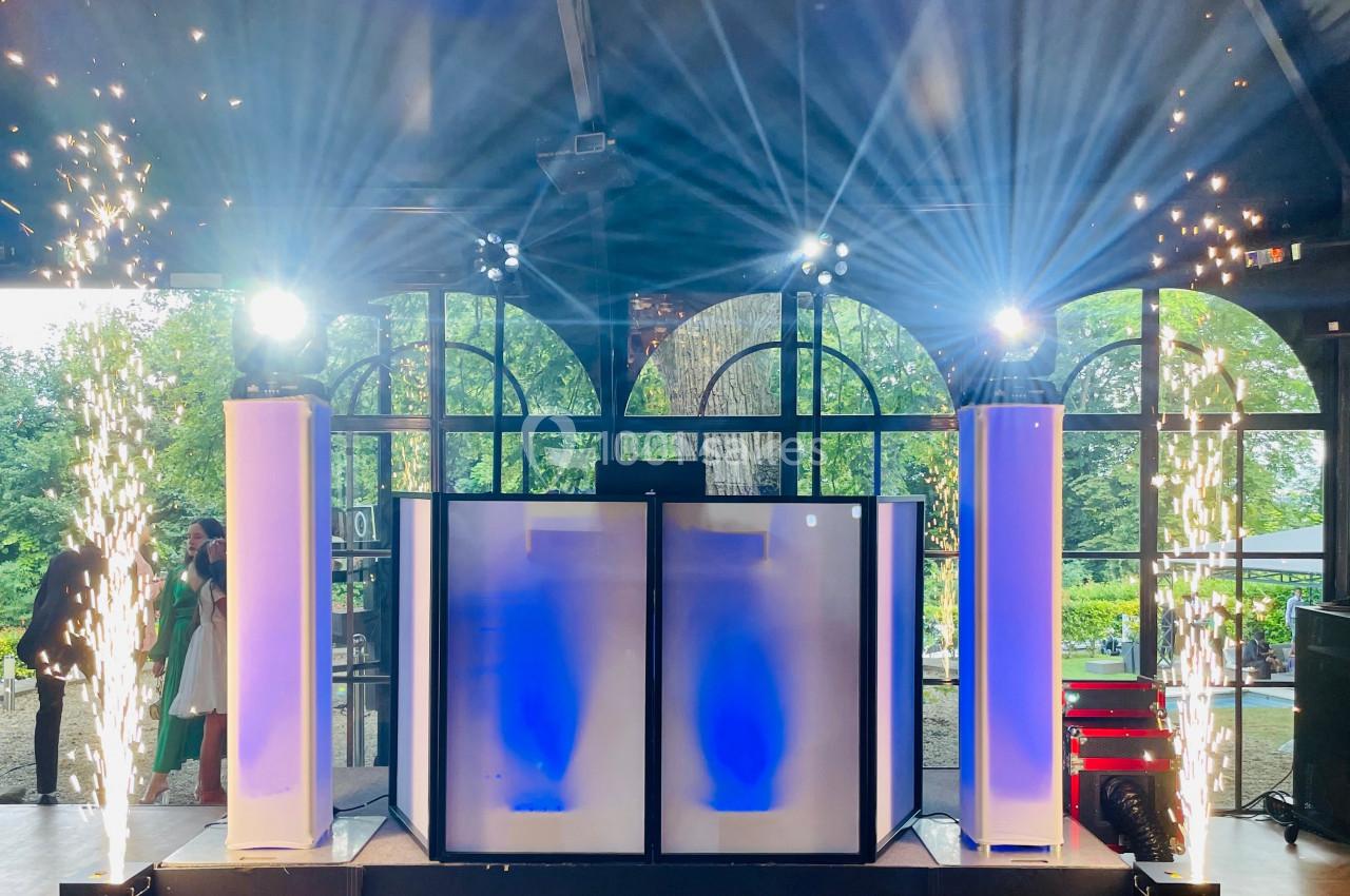 Poste de DJ éclairé avec des colonnes lumineuses, des effets pyrotechniques et une grande baie vitrée en arrière-plan.