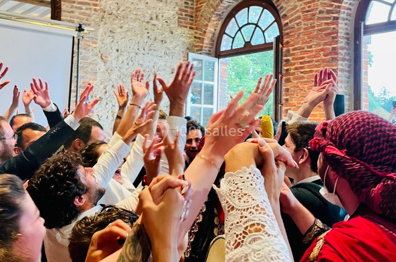 Groupe de personnes levant les bras en l'air dans une ambiance festive, près d'une fenêtre et d'un mur en briques.