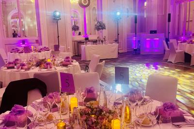 Des invités dansent joyeusement sous des lumières colorées dans une salle décorée pour une fête ou un mariage.