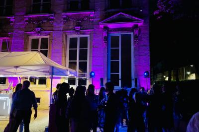 Des invités dansent joyeusement sous des lumières colorées dans une salle décorée pour une fête ou un mariage.