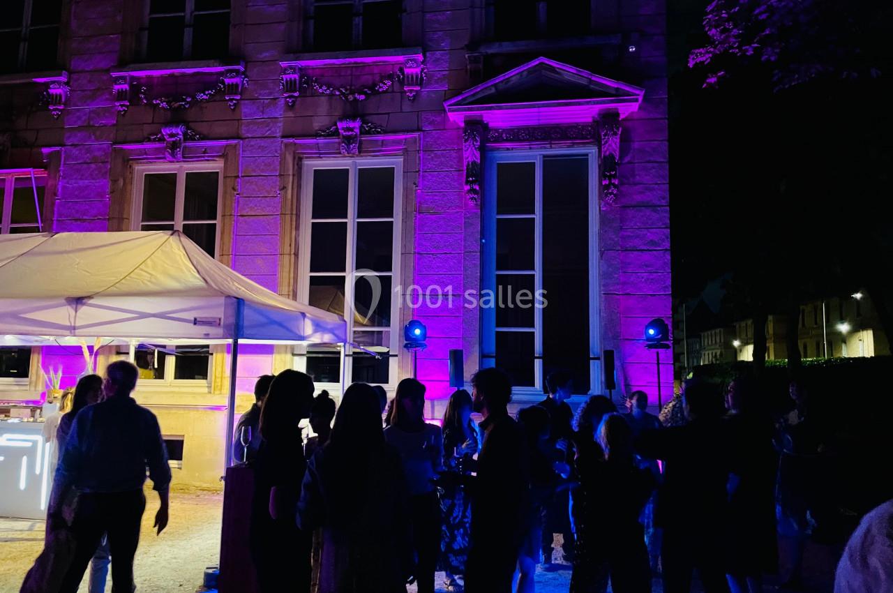 Groupe de personnes rassemblées devant un bâtiment éclairé par des lumières violettes, en extérieur de nuit.