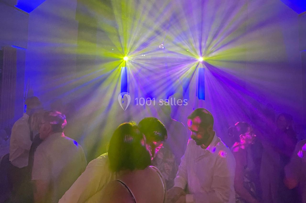 Personnes dansant sous des lumières colorées et des faisceaux lumineux dans une ambiance festive.