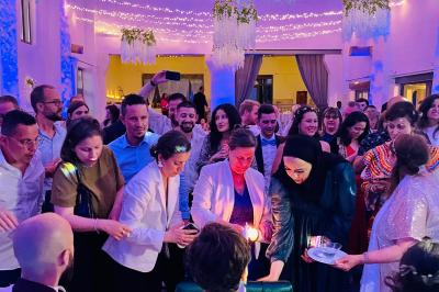 Des invités dansent joyeusement sous des lumières colorées dans une salle décorée pour une fête ou un mariage.