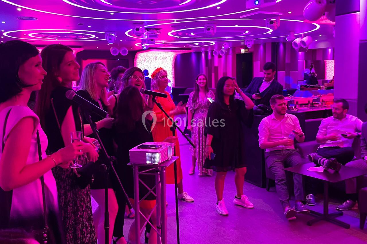 Groupe de personnes chantant au karaoké dans une salle éclairée par des lumières roses et violettes.