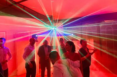 Des invités dansent joyeusement sous des lumières colorées dans une salle décorée pour une fête ou un mariage.