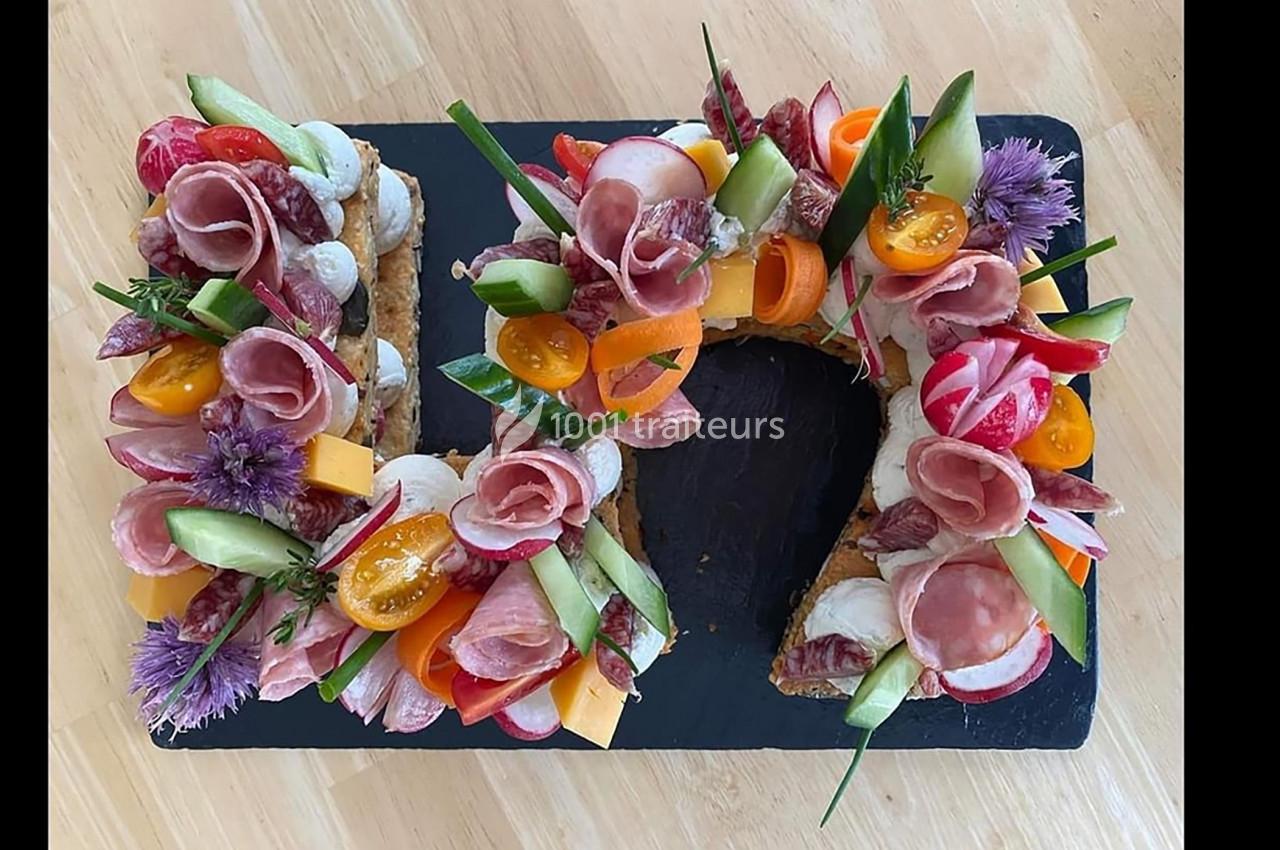Plateau en forme de couronne garni de charcuterie, légumes frais, fromage et fleurs comestibles sur ardoise noire.